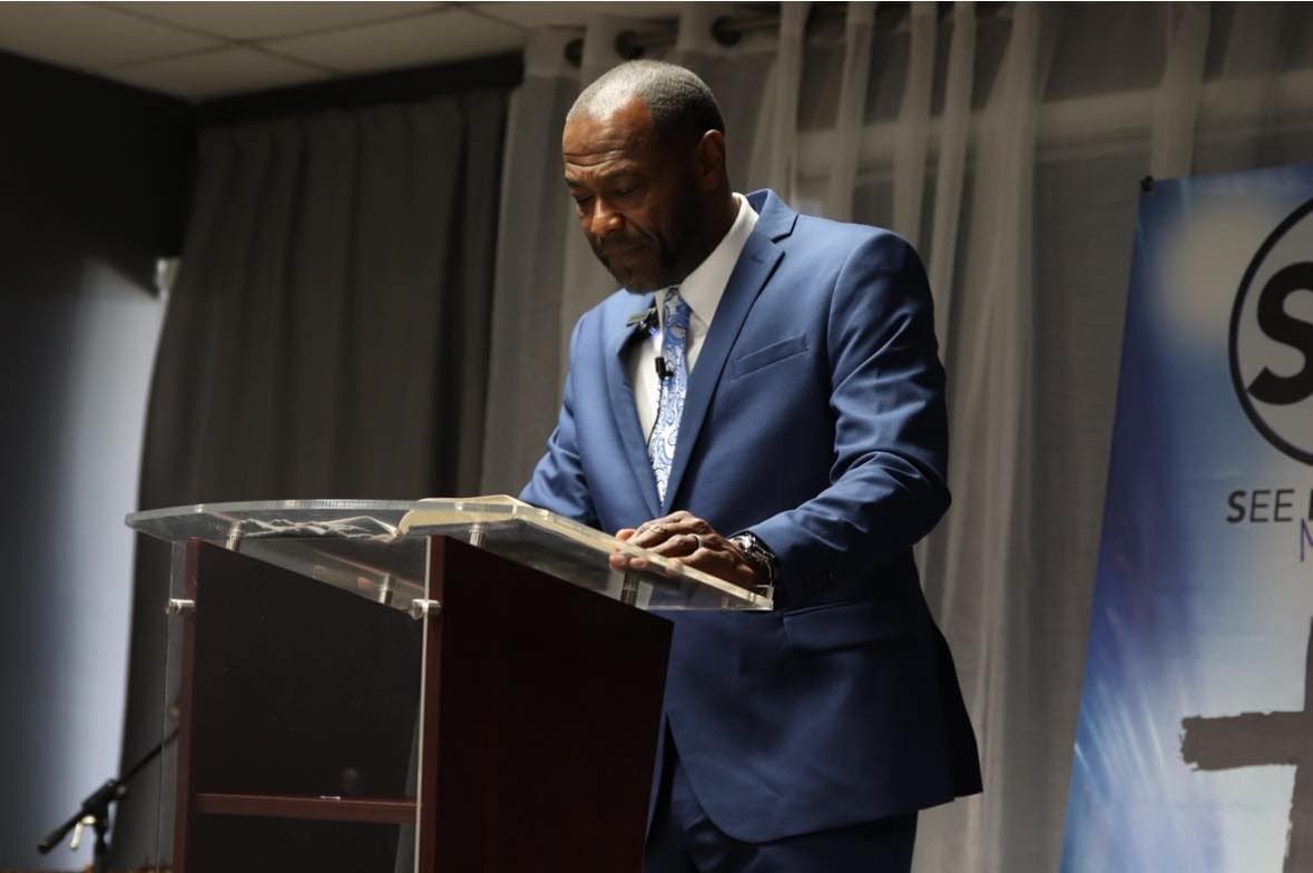 Pastor Tony Bridley preaching from an open Bible at the pulpit of See His Face Ministries