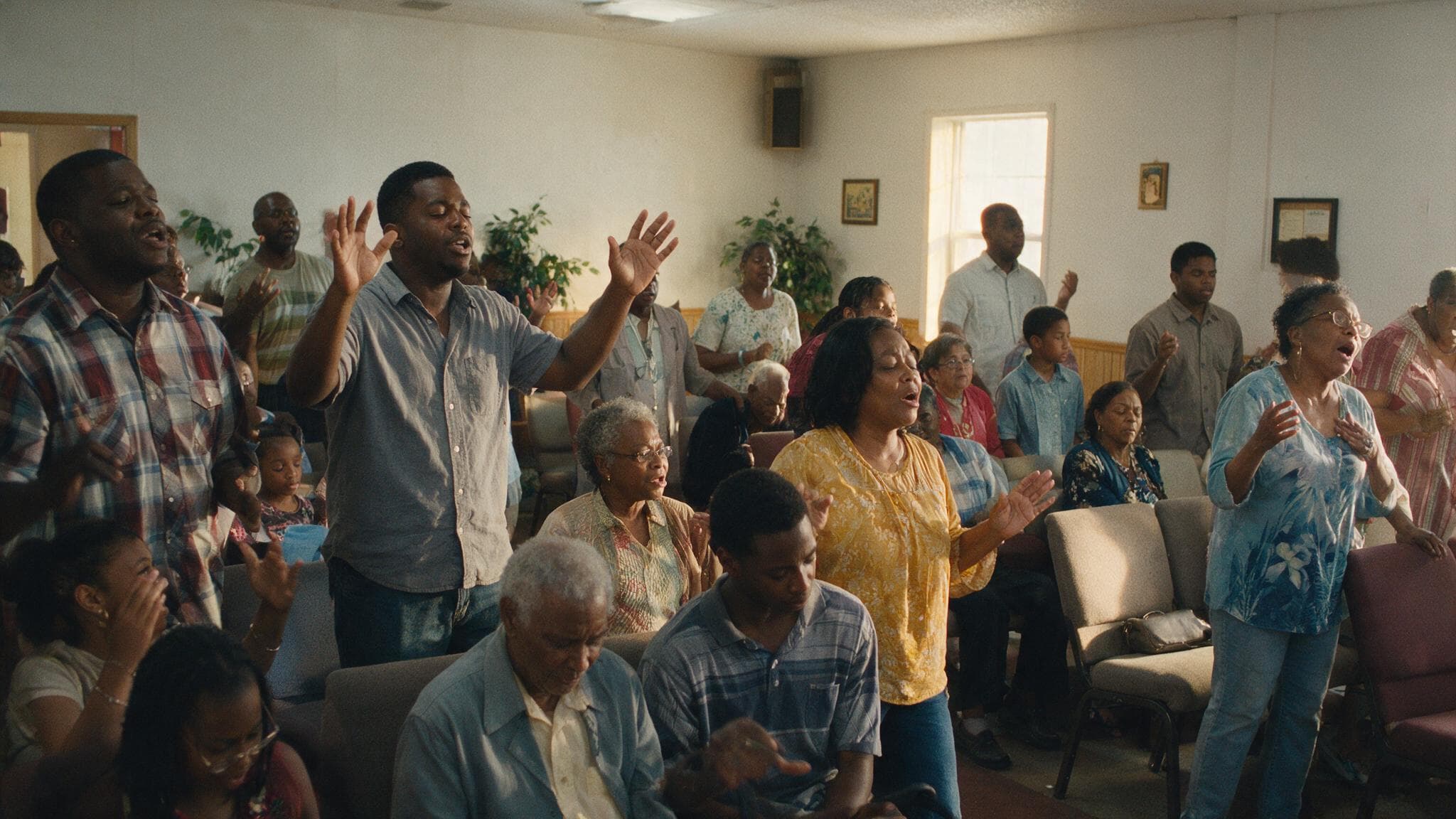 A congregation standing with hands raised in worship in a small sanctuary