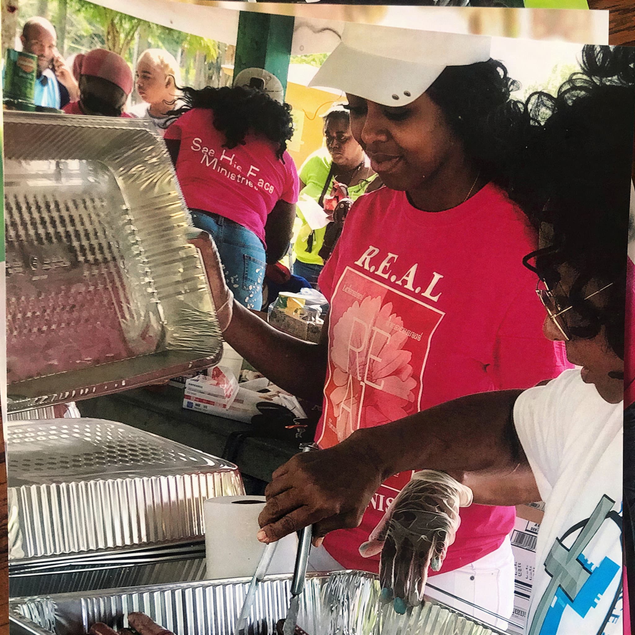 Volunteers from See His Face Ministries serving hot food from trays at a community meal