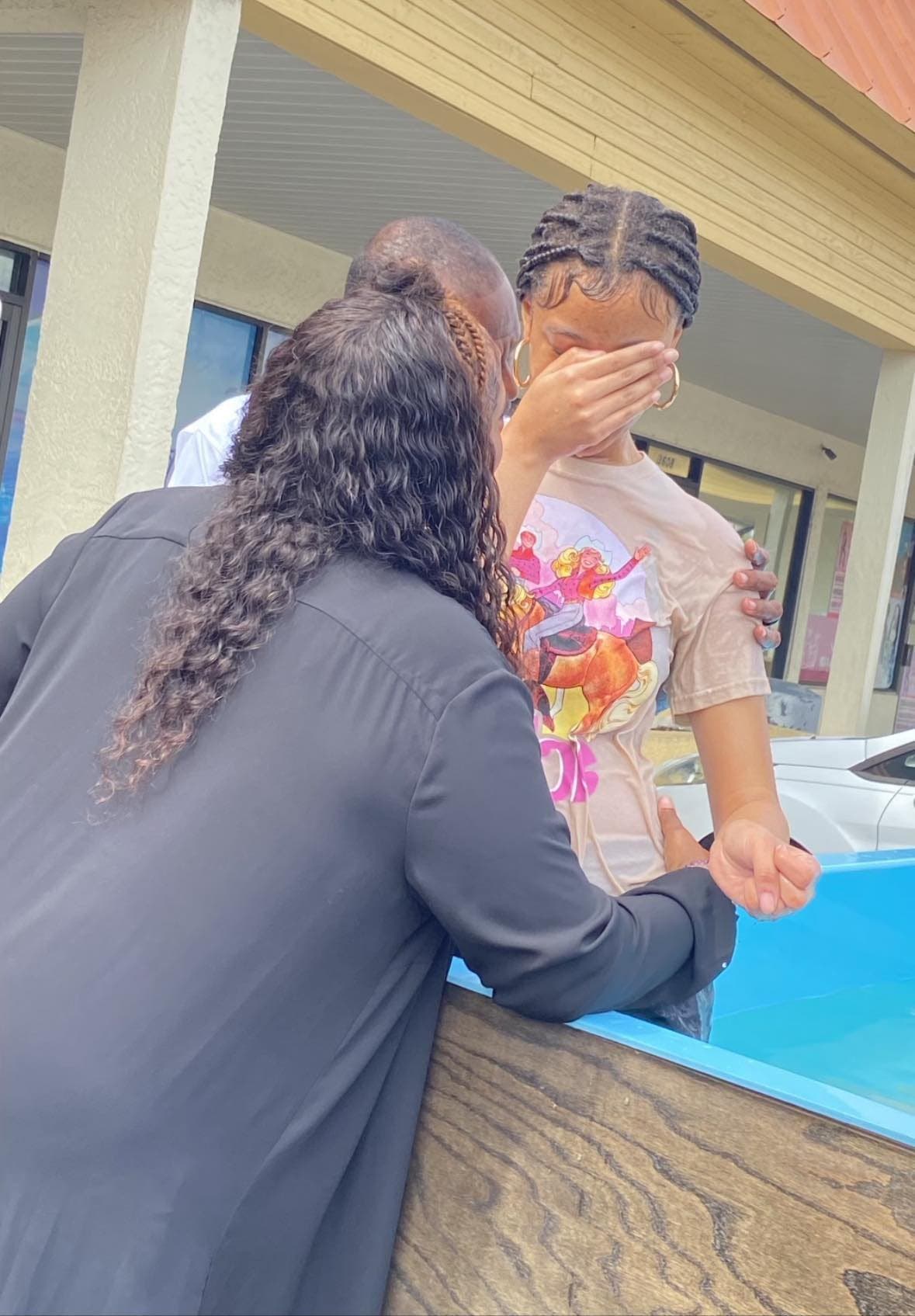 A member of See His Face Ministries resting a hand on a young woman's shoulder and praying with her beside the baptismal